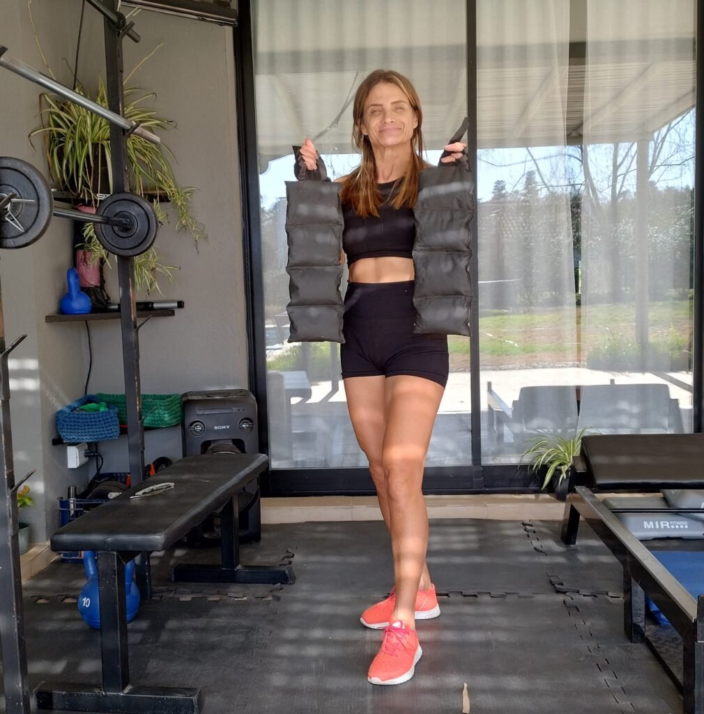 Gaby Schvap en Petit Gym mostrando un par de tobilleras de 5 kg cada una, parte del equipamiento utilizado para el entrenamiento de fuerza en SVAP Biofitness Evolutivo.