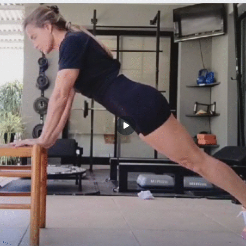 Persona realizando flexiones de brazos apoyada en una silla, paso metodológico 3 para progresar hacia la flexión completa.