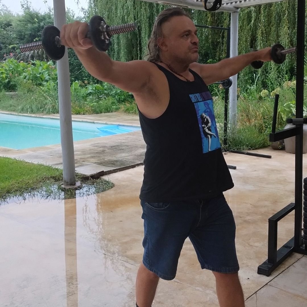 Hombre adulto realizando ejercicio de vuelo lateral con mancuernas para fortalecer hombros dentro de un entrenamiento de fuerza orientado a la salud y la funcionalidad.